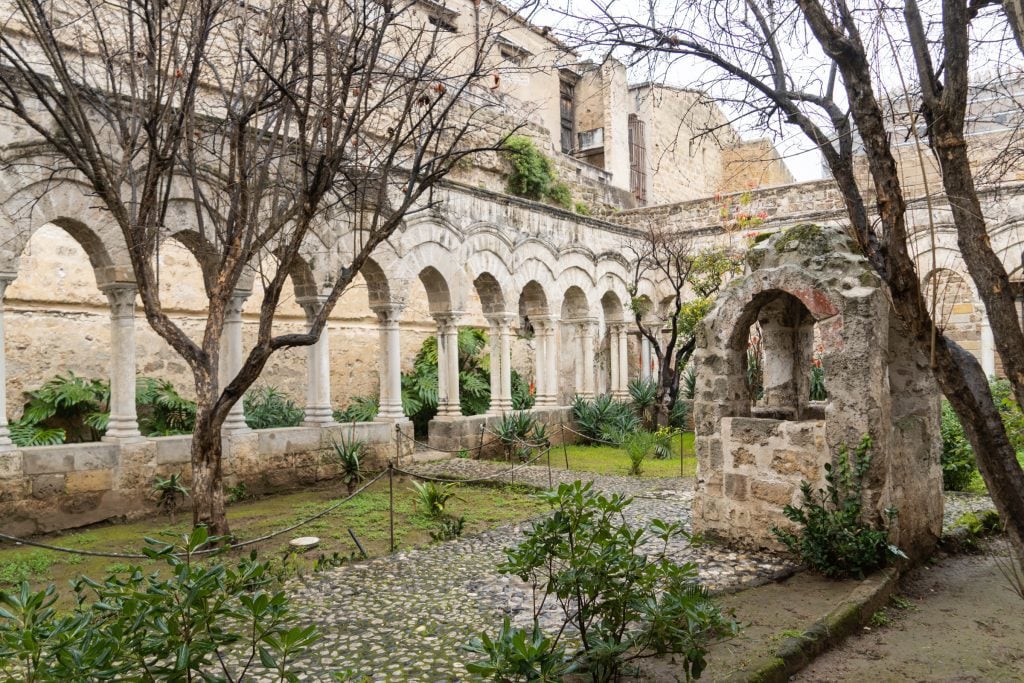 A courtyard in winter with elegant stone columns circling a green courtyard with trees.
