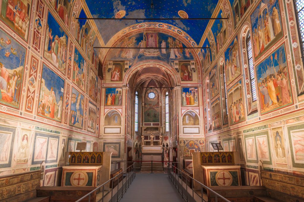 Inside of the Scrovegni Chapel with lots of colorful frescoes and a blue star-covered ceiling.
