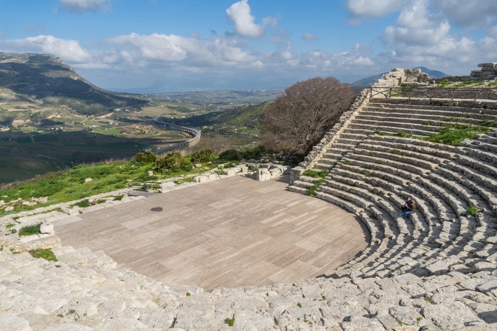 The view from a stone amphitheater perched high on a hill, hills and the ocean in the distance.