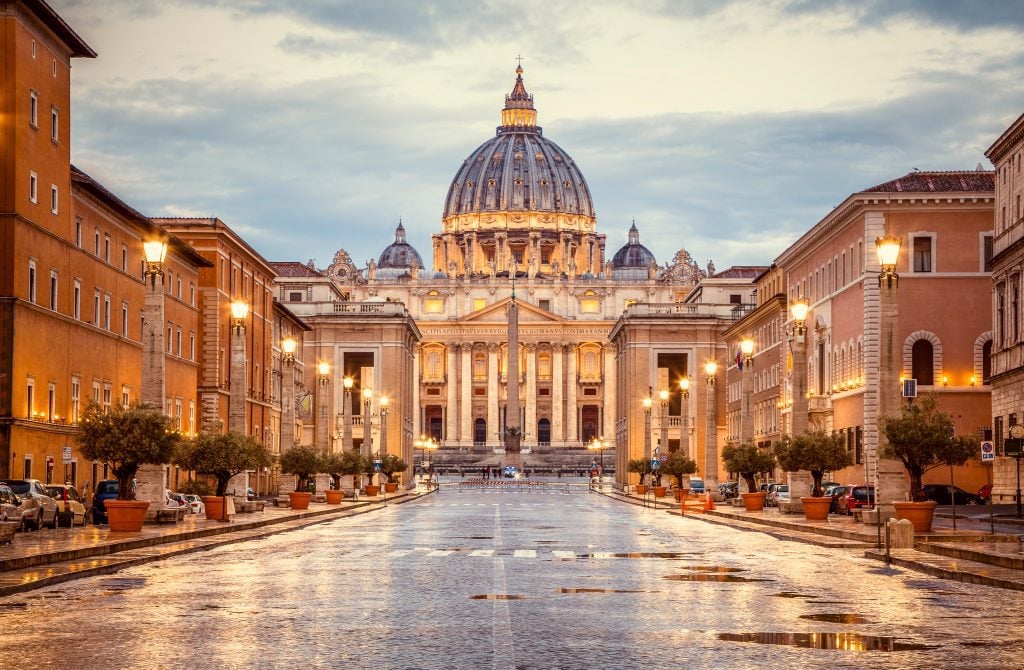 The Vatican lit up in the evening, with a cloudy sky in the background