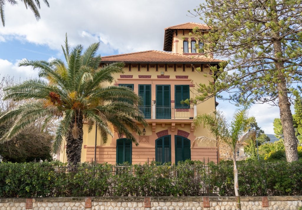 A yellow, orange, and green villa with a little turret on top, surrounded by palm trees.