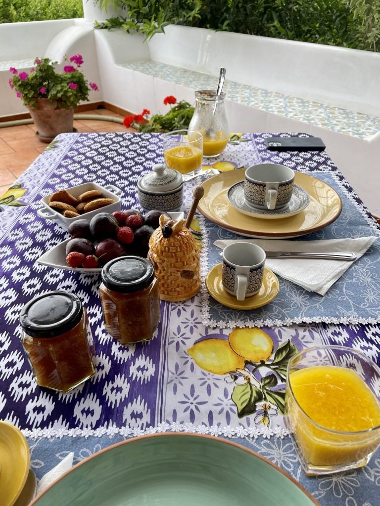 Blue and white placemat and yellow cutlery set out with fresh fruit, jams, and honey.