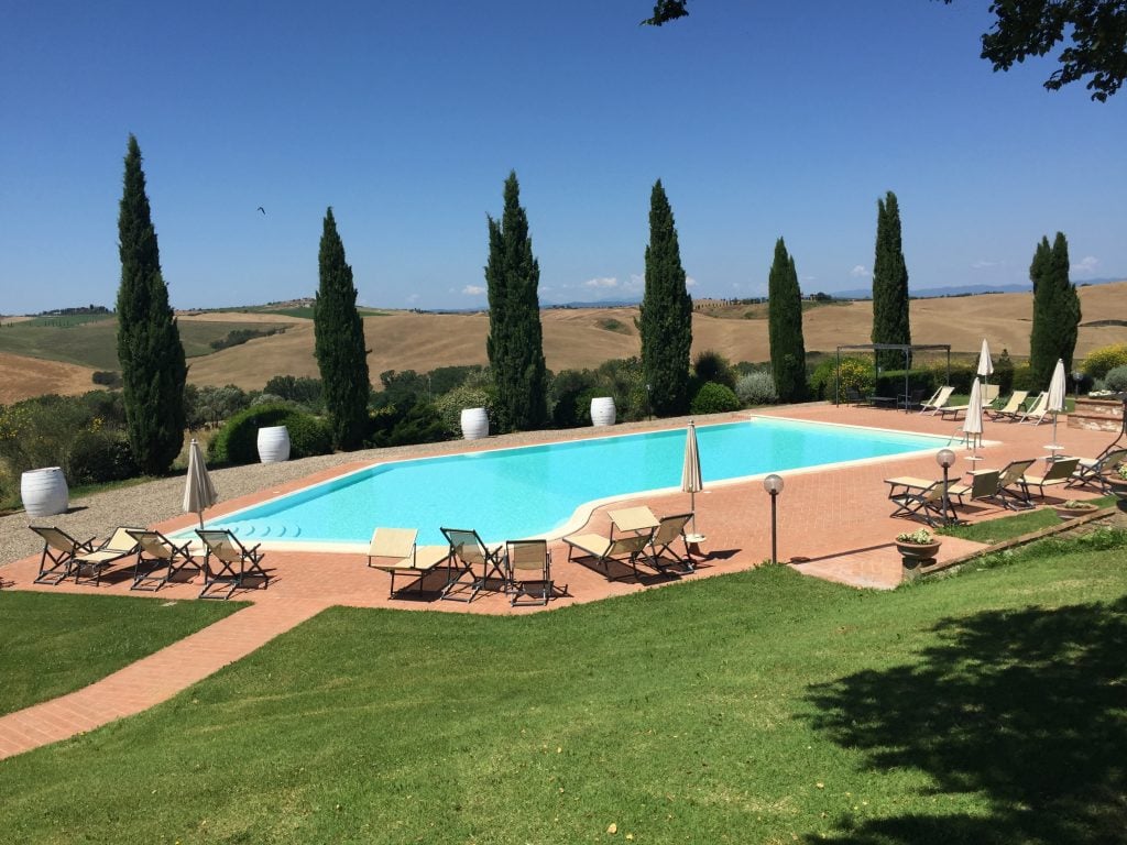 A pool surrounded by sun chairs and tall cypress trees in the Italian countryside