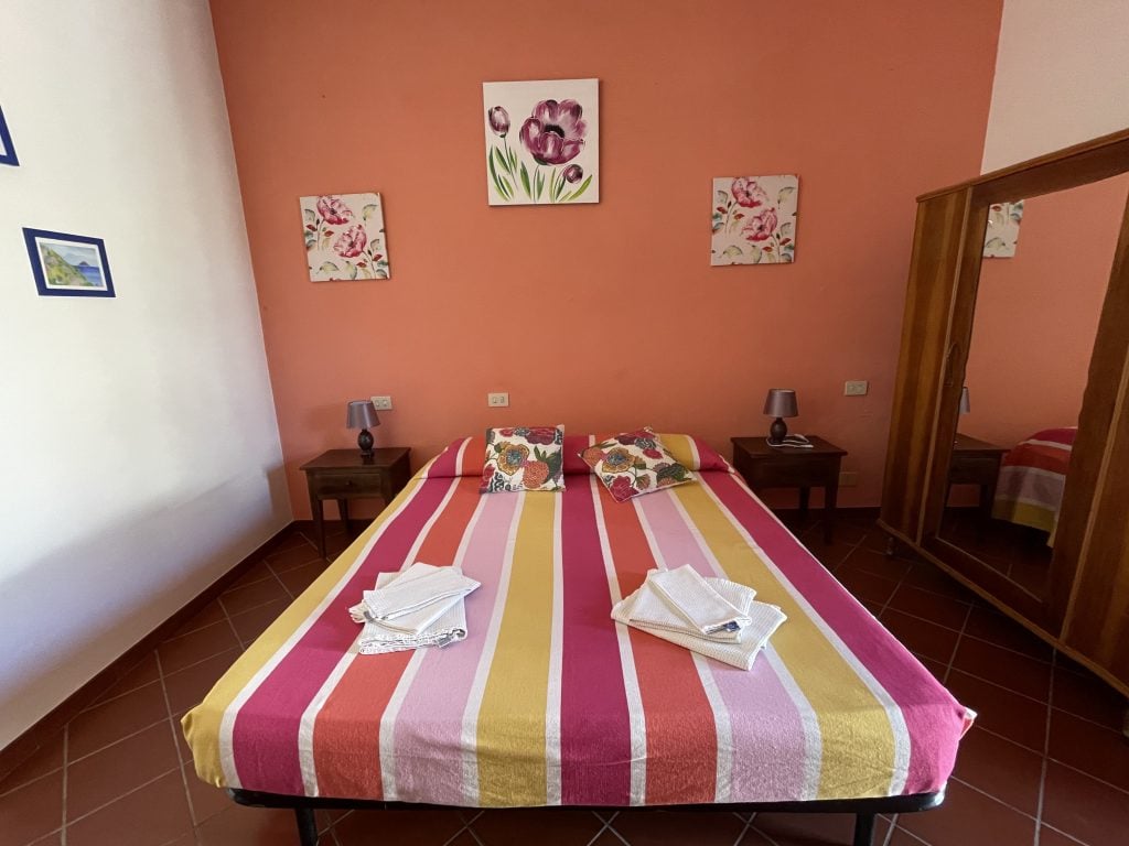 A bed in an orange room covered with bright pink and orange striped sheets.