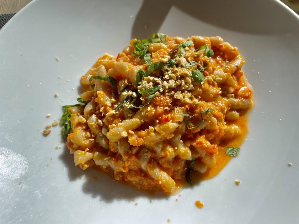 A plate of twisty pasta that looks like a phone cord, covered with tomato sauce and nuts.