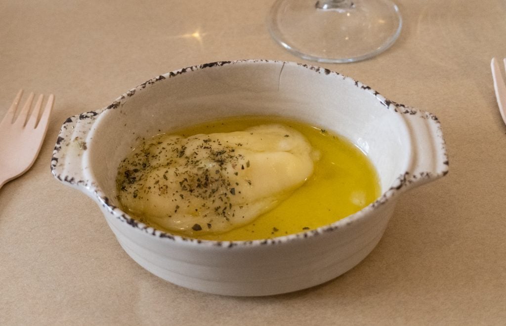 A small dish filled with melted cheese in olive oil, topped with herbs.