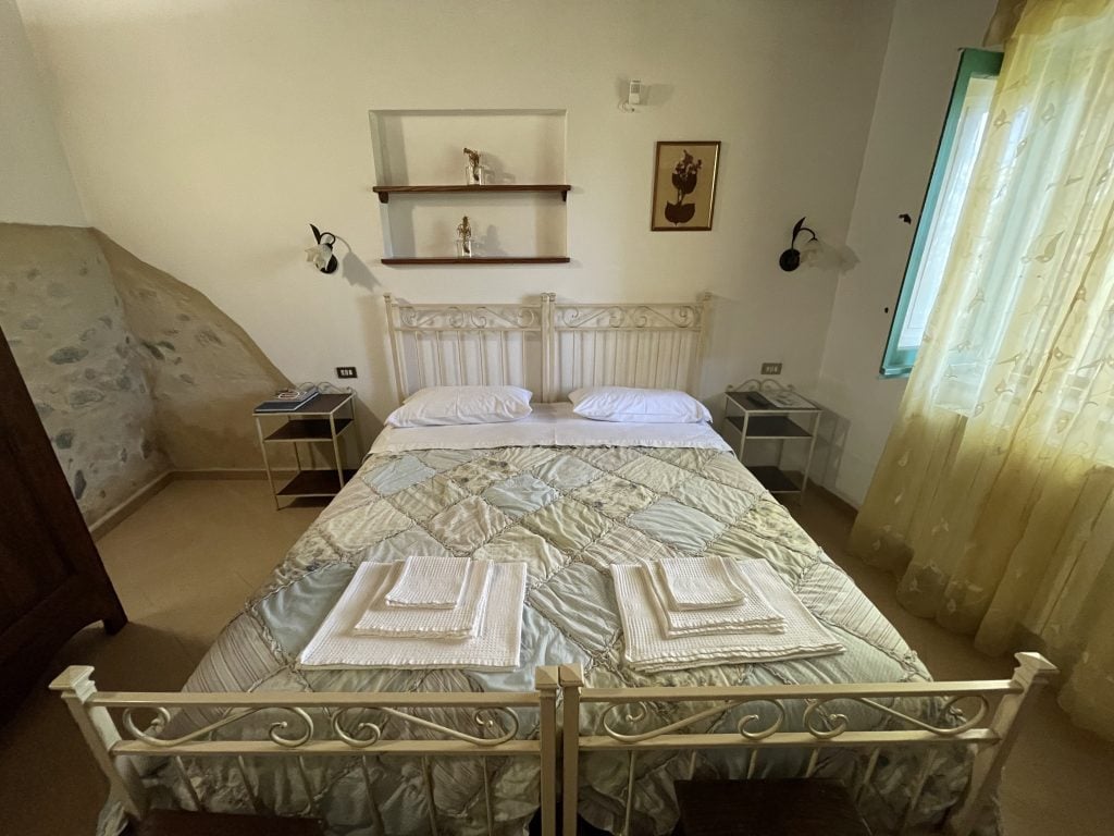 A simple bedroom with a wrought-iron bed with white linens, topped with towels of three sizes.