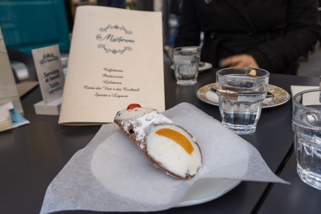 A cannoli topped with a cherry on one side and an orange rind on the other.