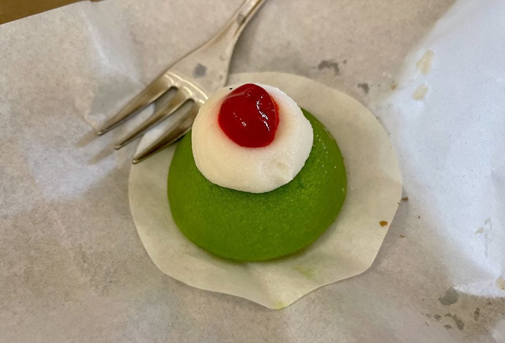 A small bright green cake topped with whipped cream and a cherry.