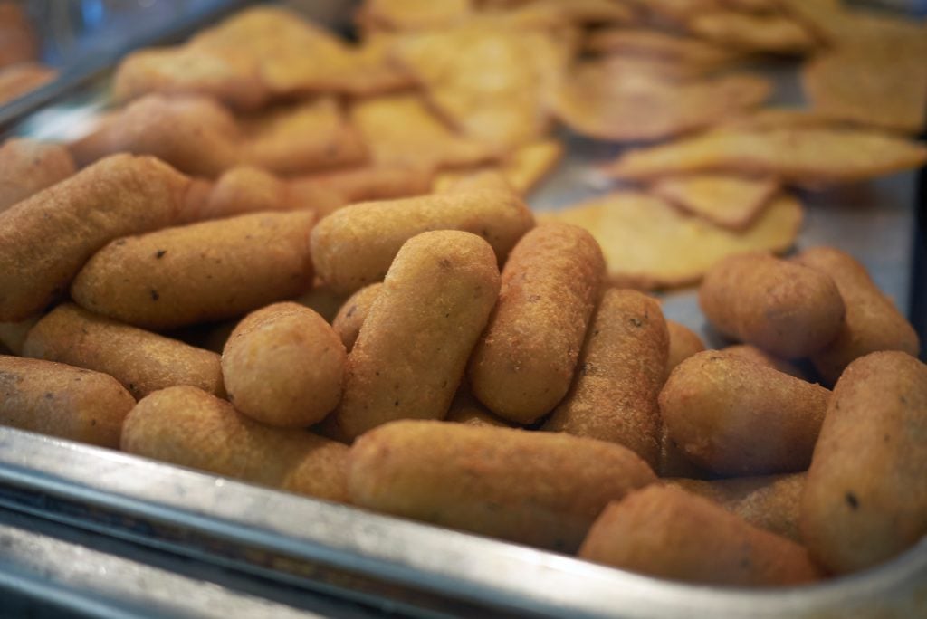 A big pile of potato croquettes in a metal pan.