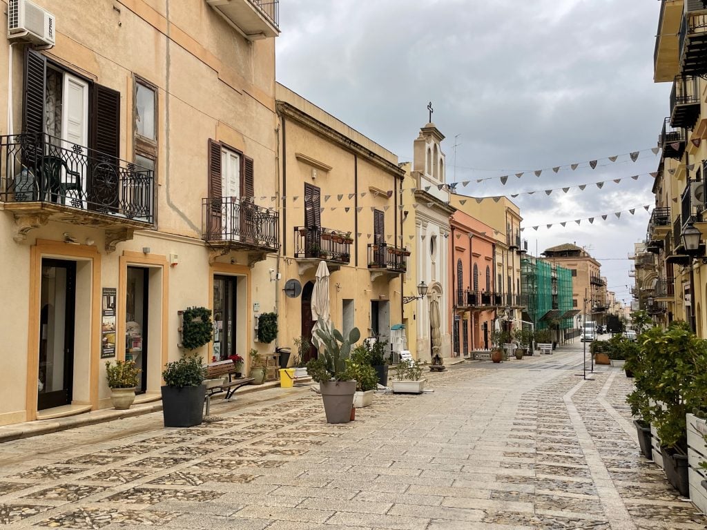 An empty street in a Sicilian village underneath a cloudy sky.