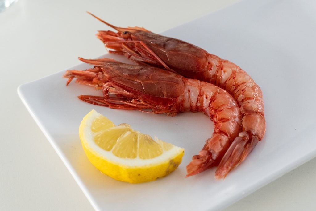 Two large red shrimps next to a lemon slice.