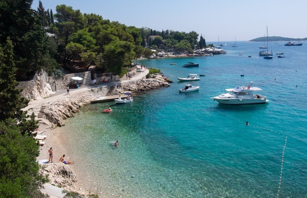 A clear turquoise bay with some boats in the water and people going for a swim in Hvar, Croatia.