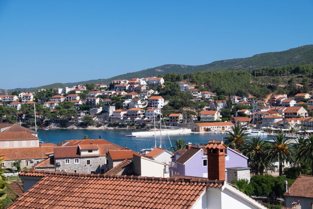 View of Hvar Town from a balcony, with lots of white cottages with orange roofs nestled into the hills, overlooking the sea.