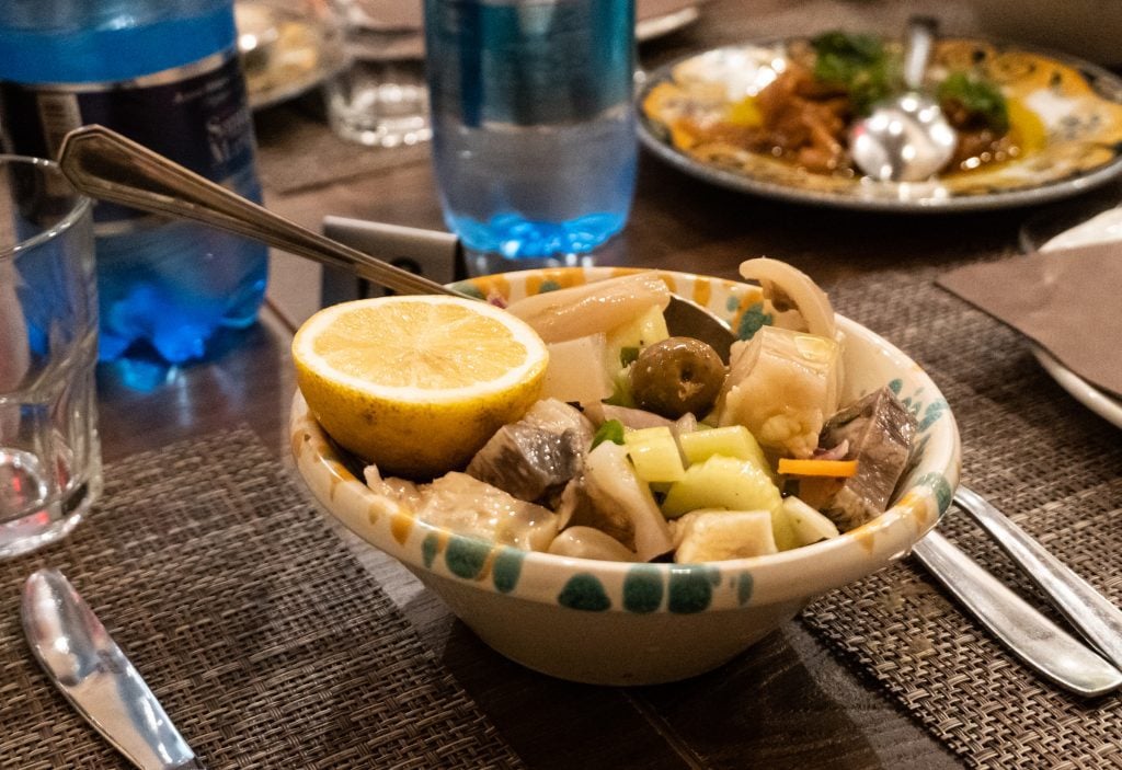 A salad of chunks of veal cartilage and vegetables with a half of a lemon.