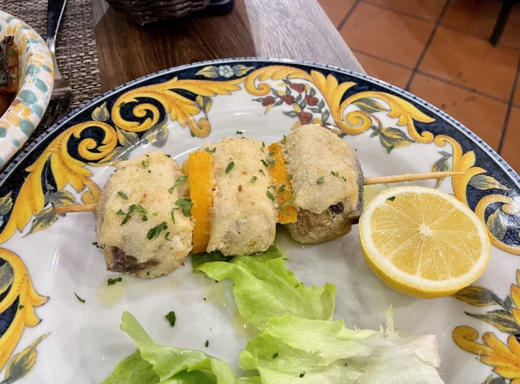 Three kabobs of swordfish wrapped around breadcrumbs on a spear.