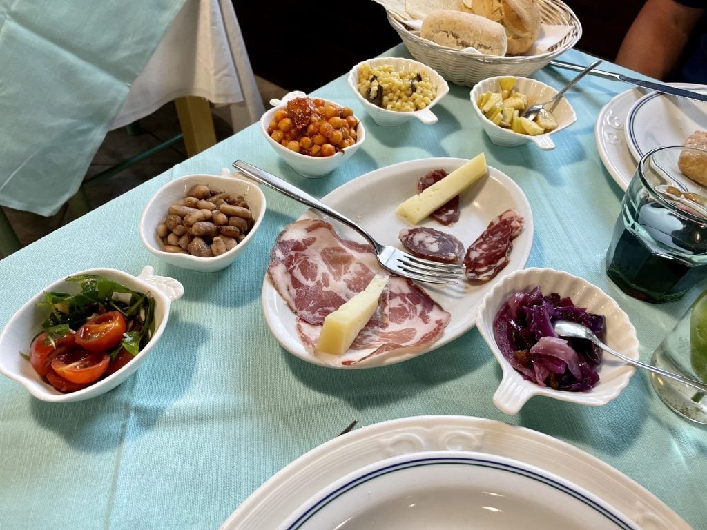 A plate covered with deli meats and cheese wedges next to small bowls with various different vegetables.