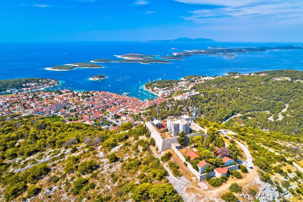 An aerial view of a small fort on the center of an island, spreading out to the town below and islands in the distance.