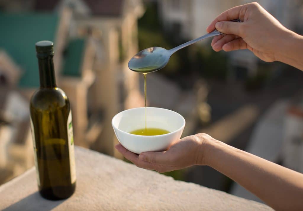 A spoon dripping olive oil into a white ramekin.
