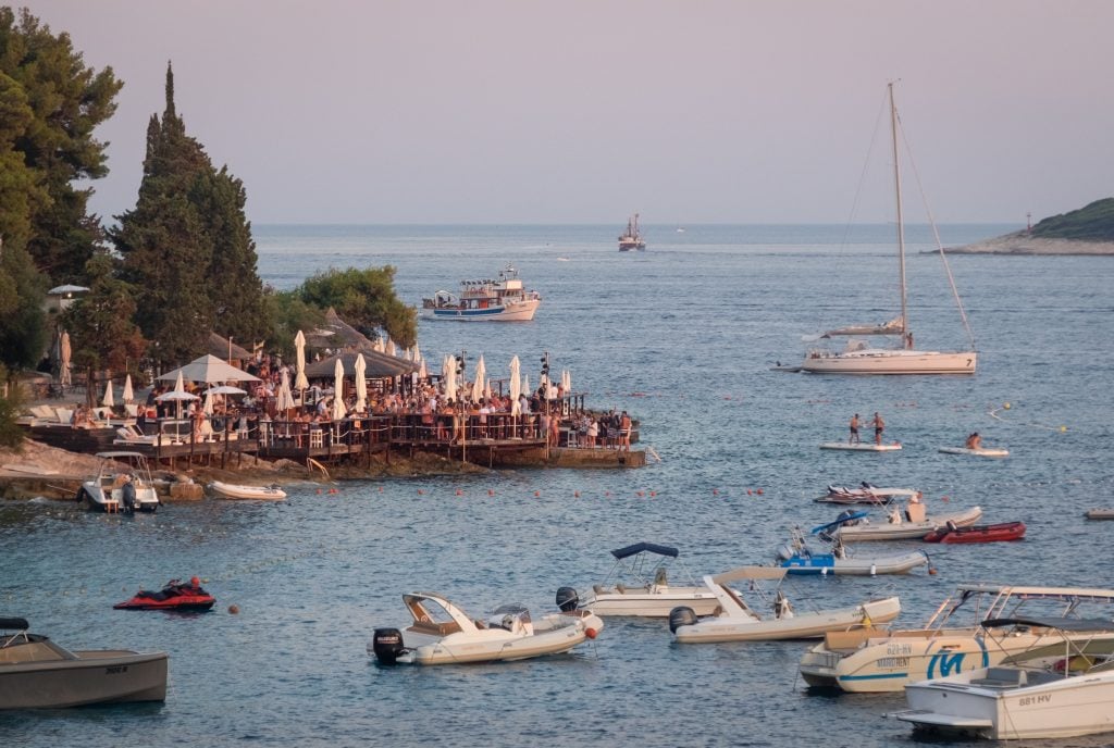 A packed bar perched on the corner of a walkway, on the edge of the sea.