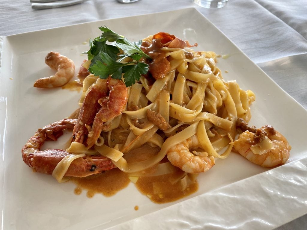 A plate of pasta topped with shrimp and bright orange bits of sea urchin.