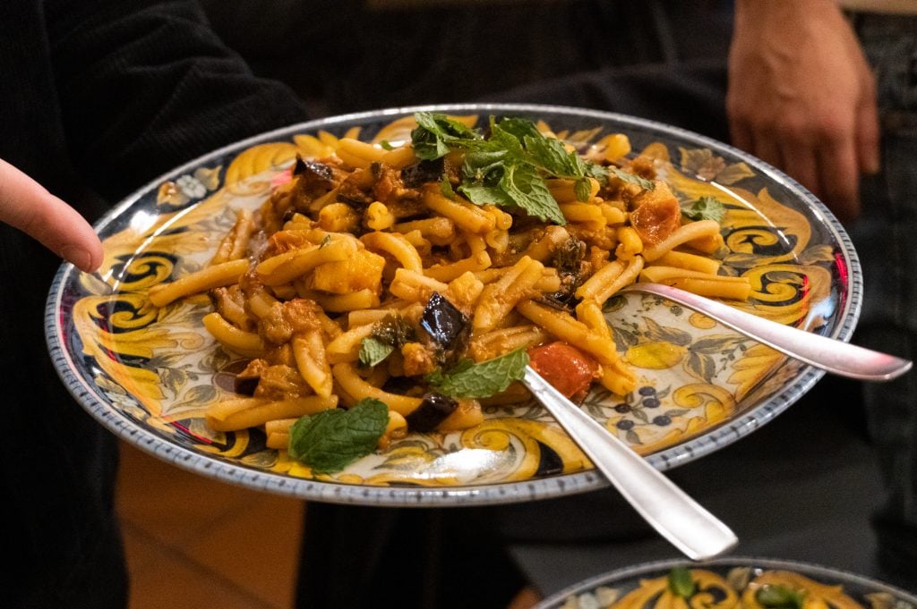 A plate of pasta topped with eggplant, swordfish, tomatoes, and mint.