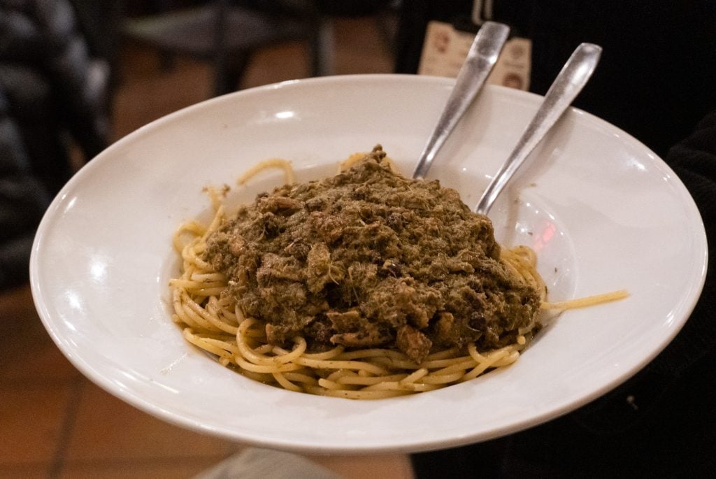 A plate of pasta topped with a brown sauce of sardines and anchovies.