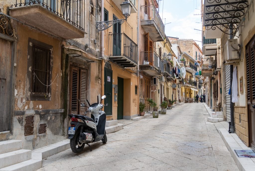 A quiet, empty street in Italy with a motorbike parked.