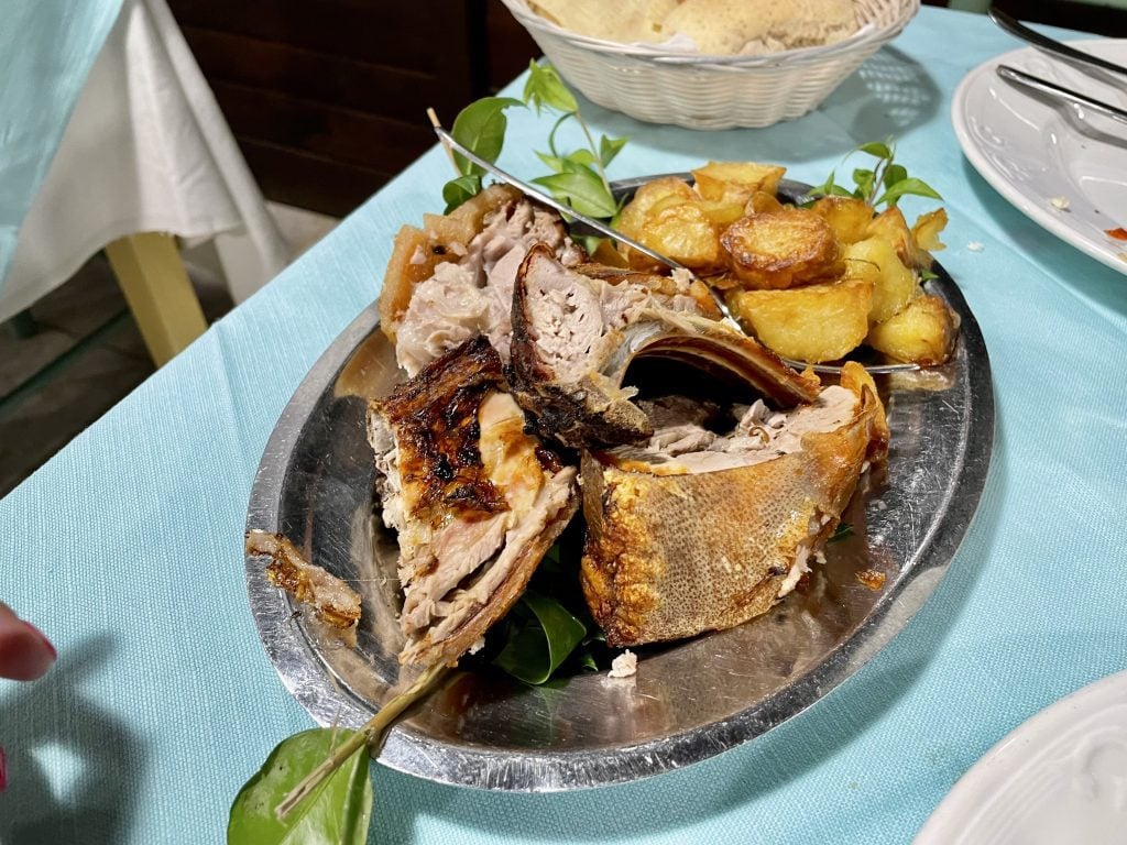 A metal plate topped with roasted pork and roasted potatoes.