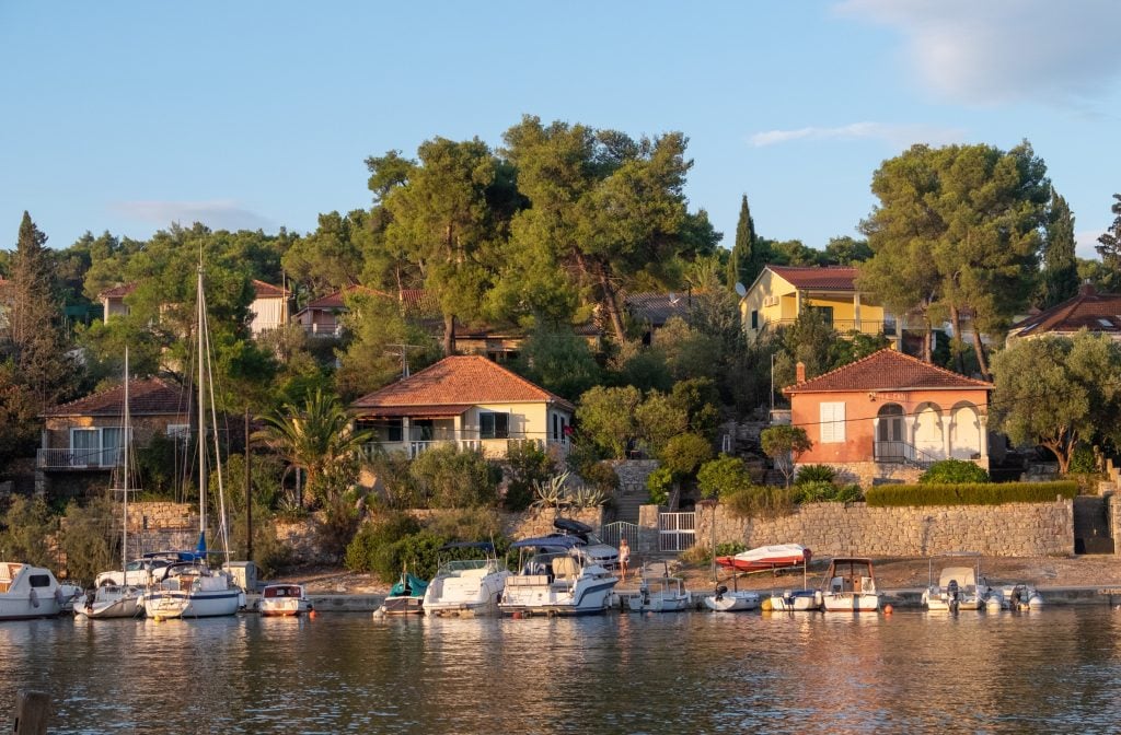 A quiet seaside village with villas set amongst the trees and sailboats docked below.