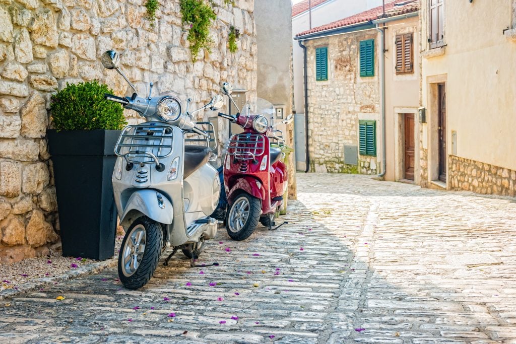 Two scooters parked on the street in a stone old town in Croatia.