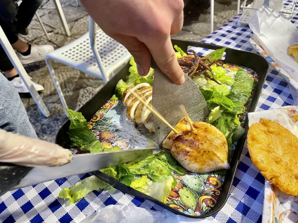 Hands slicing a big grilled squid on a plate.