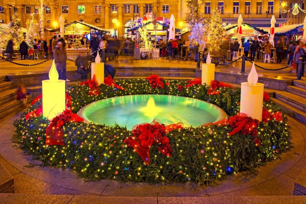 An advent wreath with candles lit in front of Christmas market stalls in Zagreb.