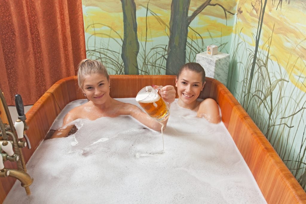 Two young women in a beer bath, each holding up a glass of beer.