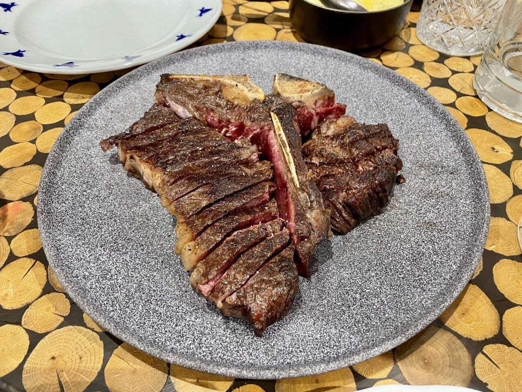 A T-bone steak, glistening and sliced off the bone into slices.