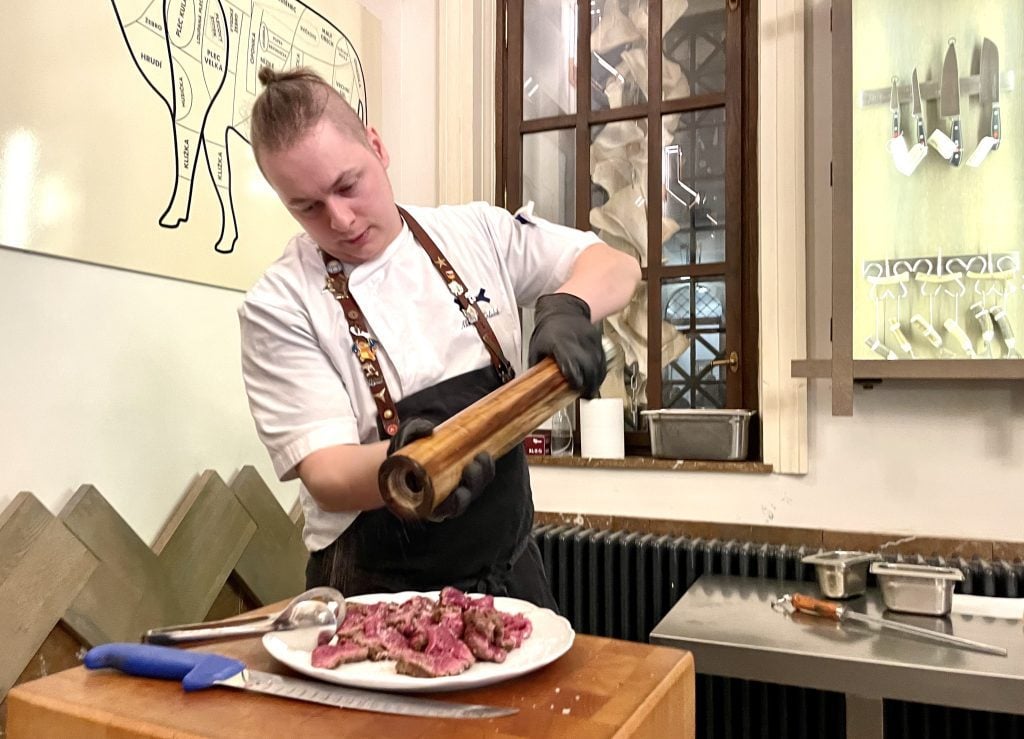 Butcher Matthew grinds pepper over a plate of carpaccio.
