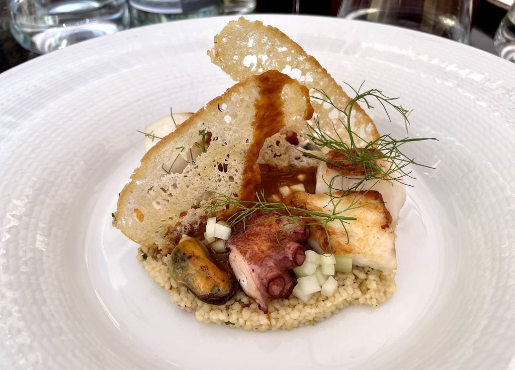 A fancy plate topped with couscous, shellfish, and artfully arranged crostini slices.