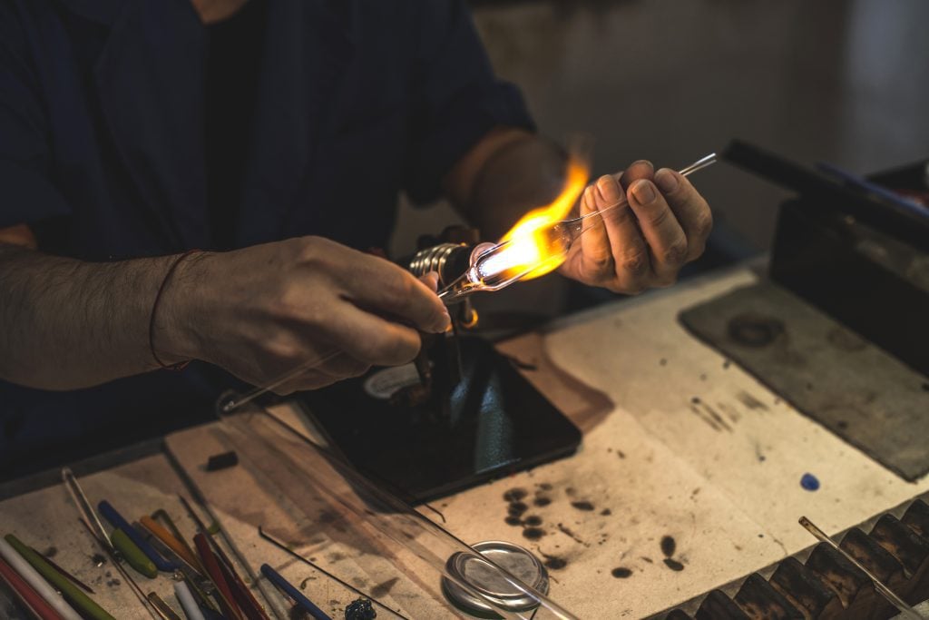 A person using a flame to shape a glass test tube into a sculpture.