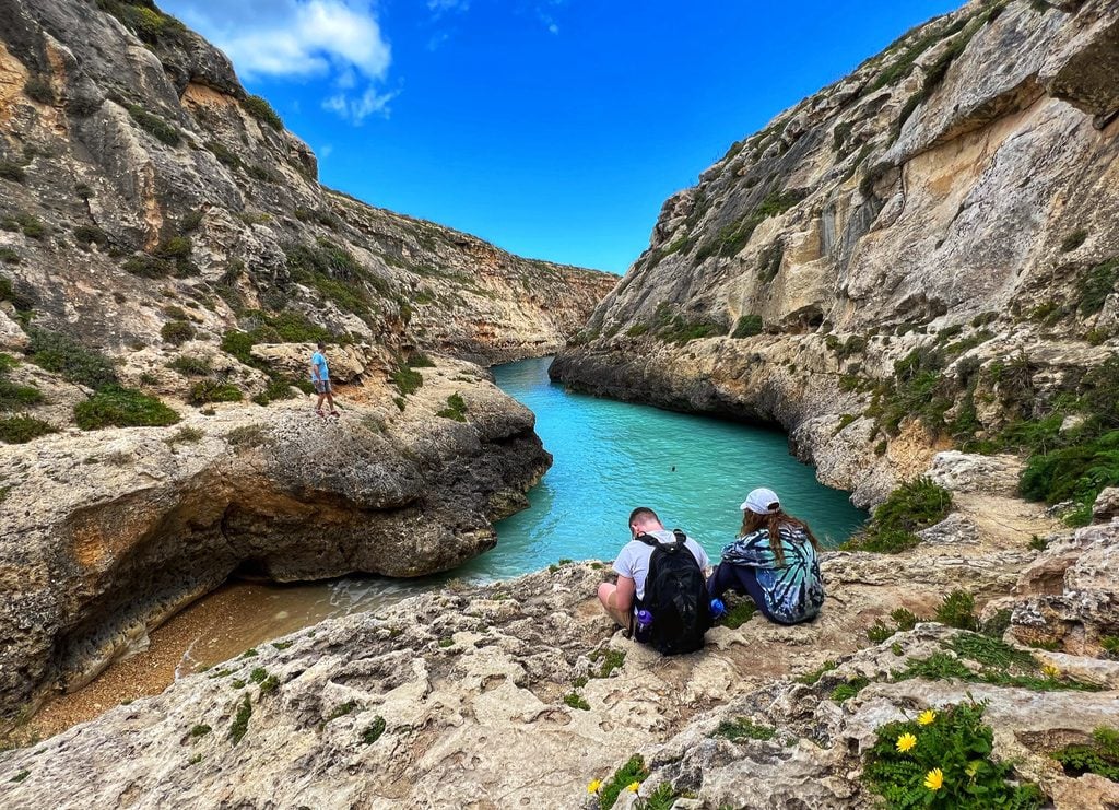 Two people sitting at the Wied il-Ghasri gorge on Gozo, Malta with a clear blue sky in the background
