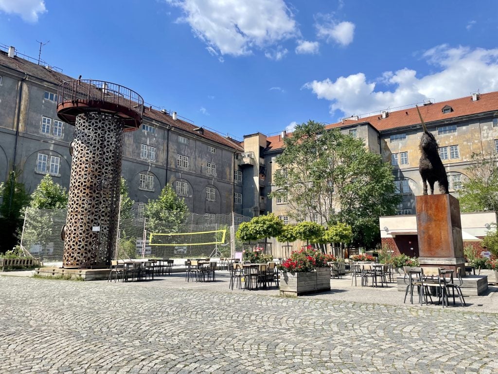 A courtyard filled with sculptures, chairs, and a beach volleyball pitch.