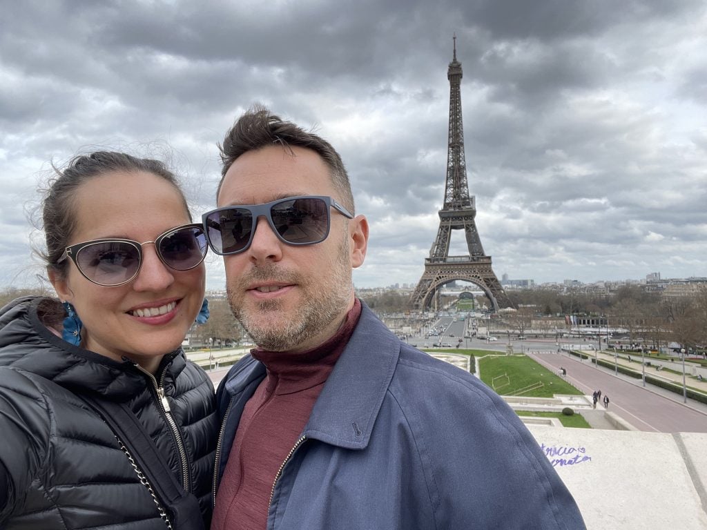 Kate and Charlie taking a selfie, wearing sunglasses, in front of the Eiffel Tower.