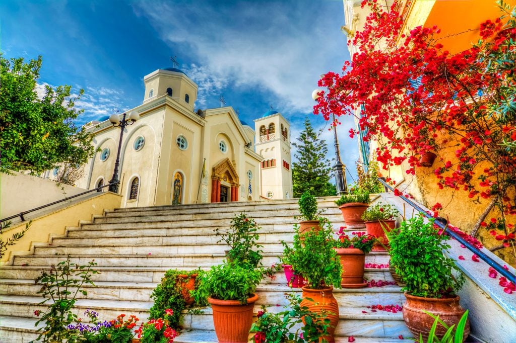 Plants on a stairway in Kos, with a red tree against a yellow building on the right and the sky in the background