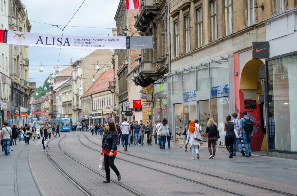 A woman crossing a busy street with tram tracks in Zagreb.