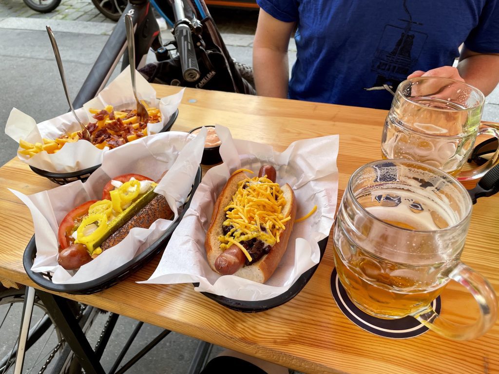 Two hot dogs covered with lots of toppings, half-consumed beers, and a plate of chili cheese fries.