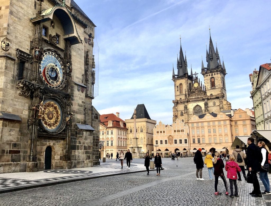 Old Town Square in Prague, surrounded by candy-colored buildings, gothic church towers, and the metal-layered astronomical clock.