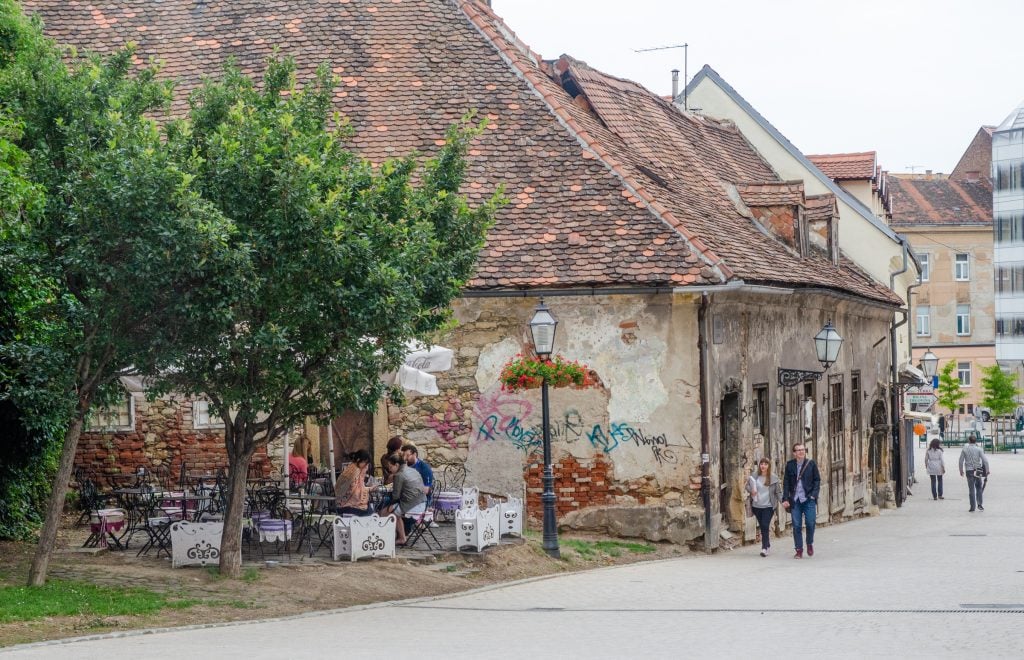 A couple walking past a dilapidated looking brick house now housing a cafe.