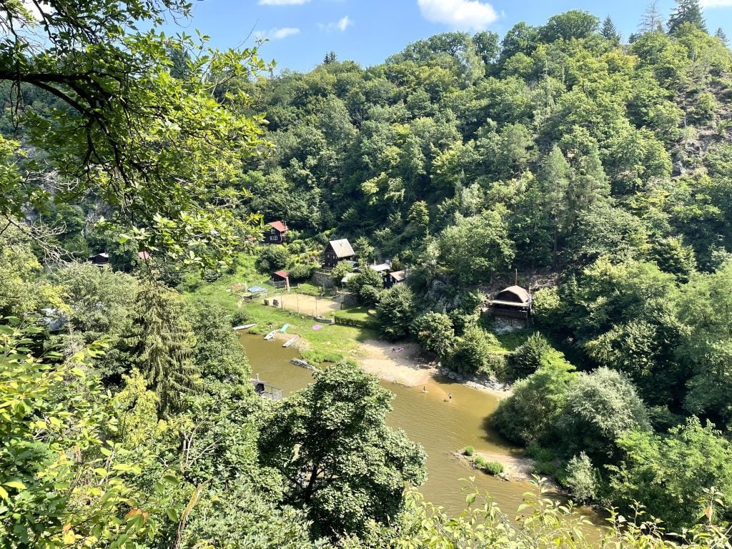 A view looking over a river running through the woods, tiny wooden cabins on shore.
