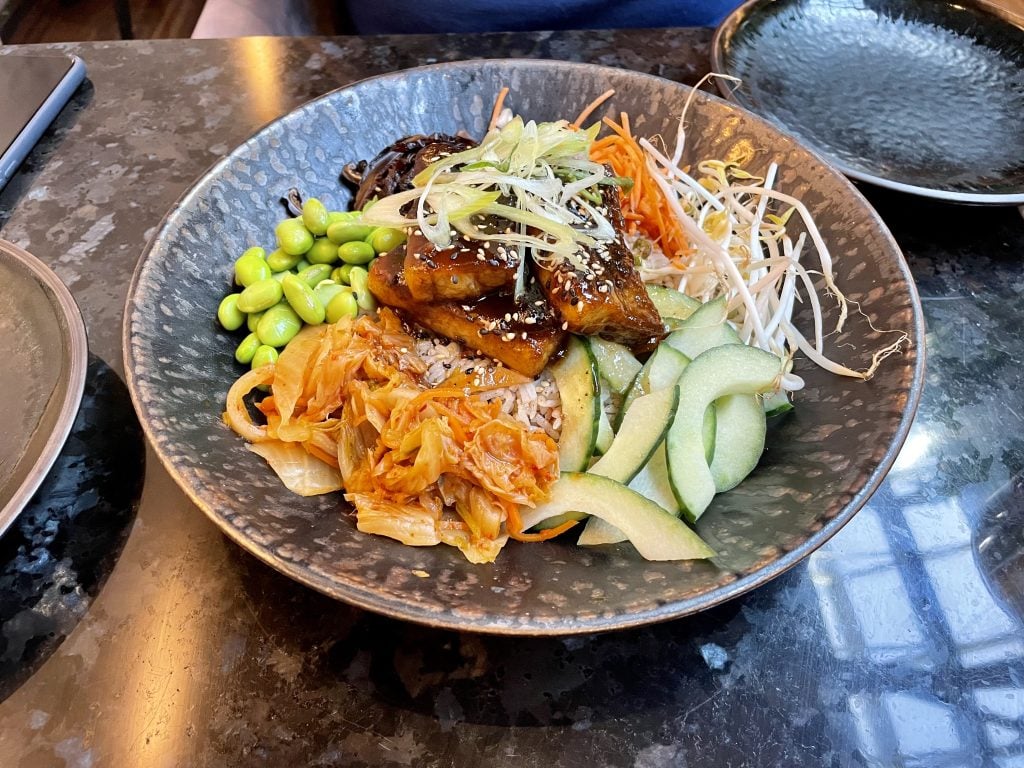A Korean bibimbap topped with lots of fresh vegetables and barbecued pork belly.