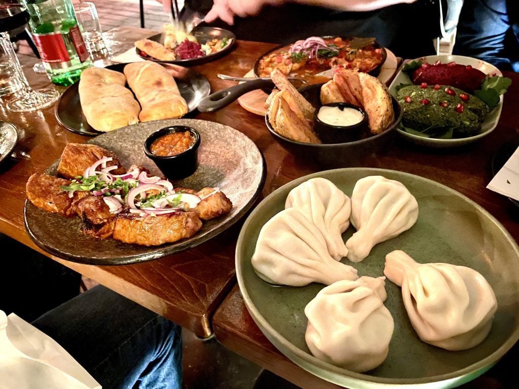 Plates covered with dumplings, eggplant rolls, fresh bread, and walnut dips.