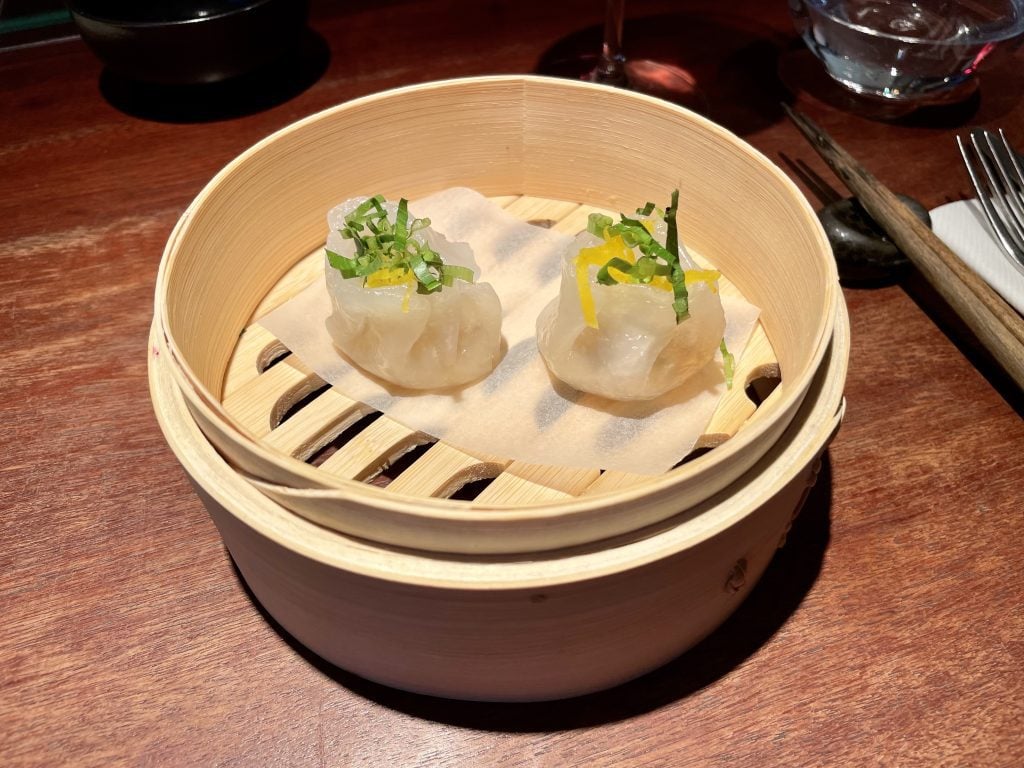 A bamboo steamer dish filled with two tiny rice paper dumplings.